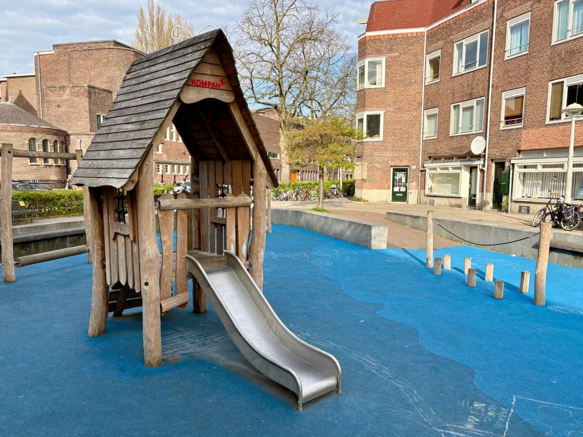 Small wooden play house with slide set in residential area on blue-floored play ground