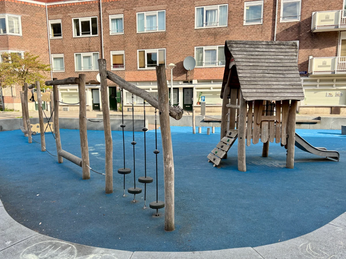 Wooden play house with slide next to wood and rope balance obstacle course set on blue rubber play surface