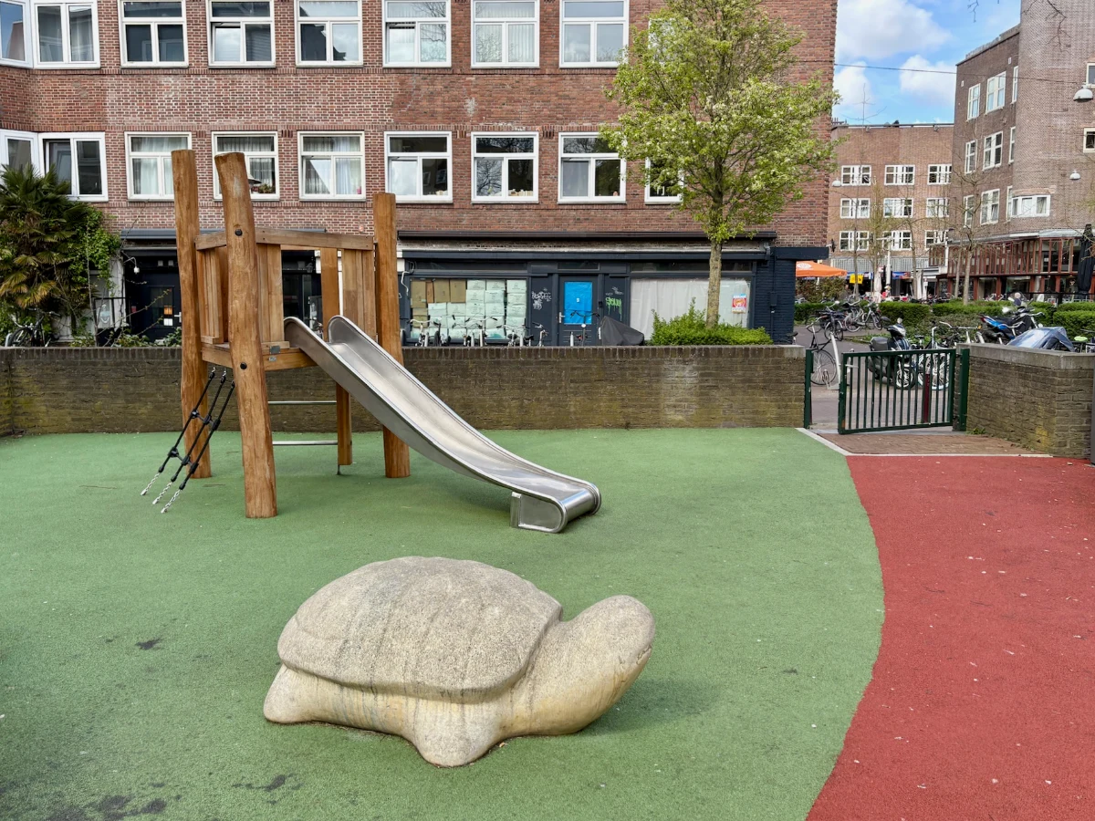Small wooden climbing tower with metal slide and concrete turtle on red and green astroturf playground