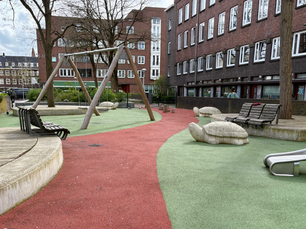 Playground with swing set, concrete turtles, and benches on red and green astroturf