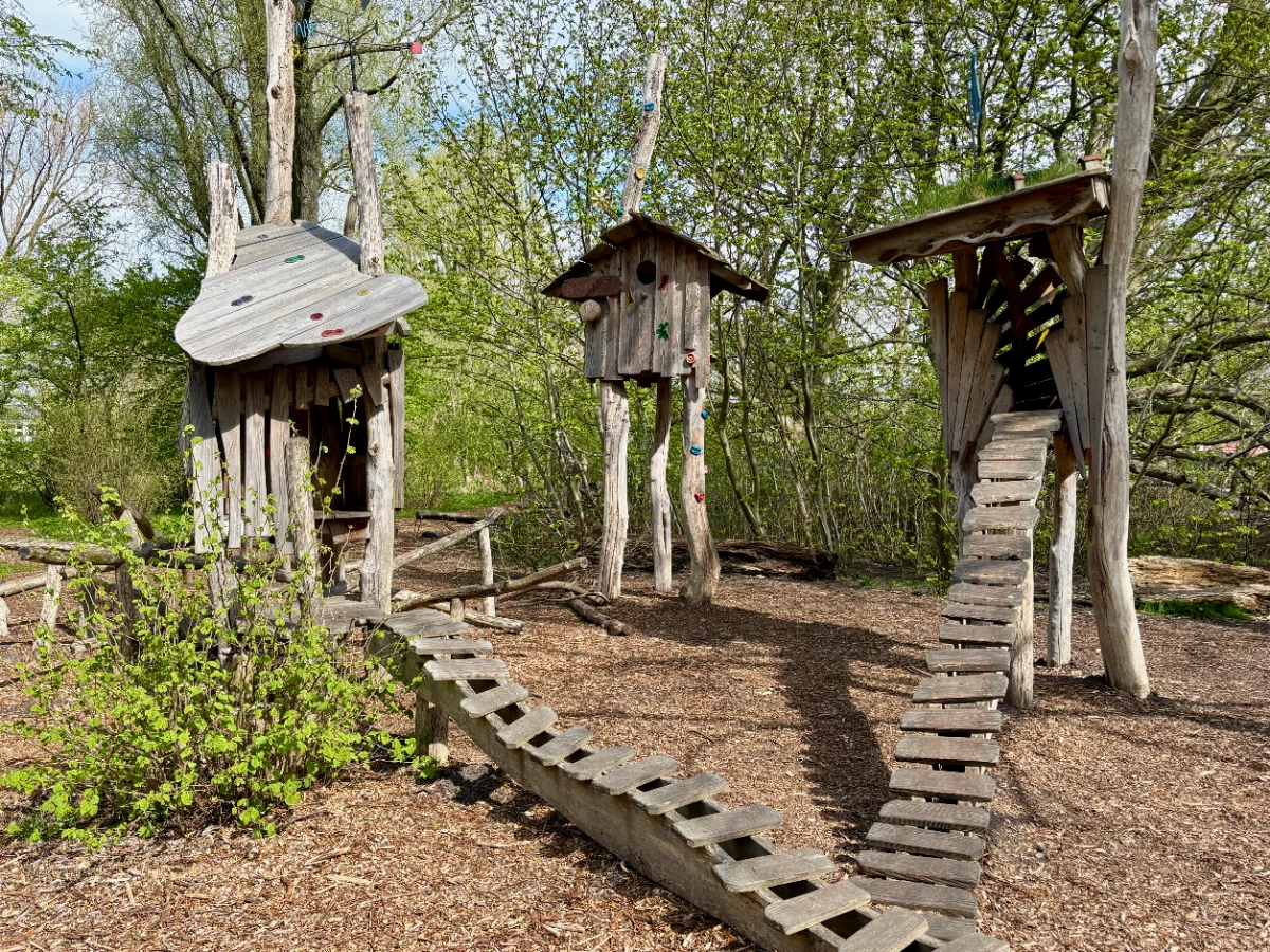 Three whimsical wooden treehouses with ladders and climbing holds in a forest