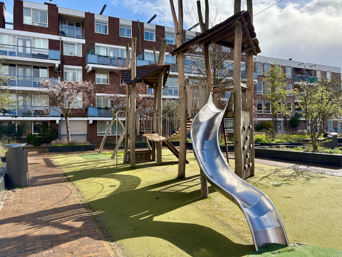 Wooden climbing structure with bridge connecting two towers and curvy metal slide