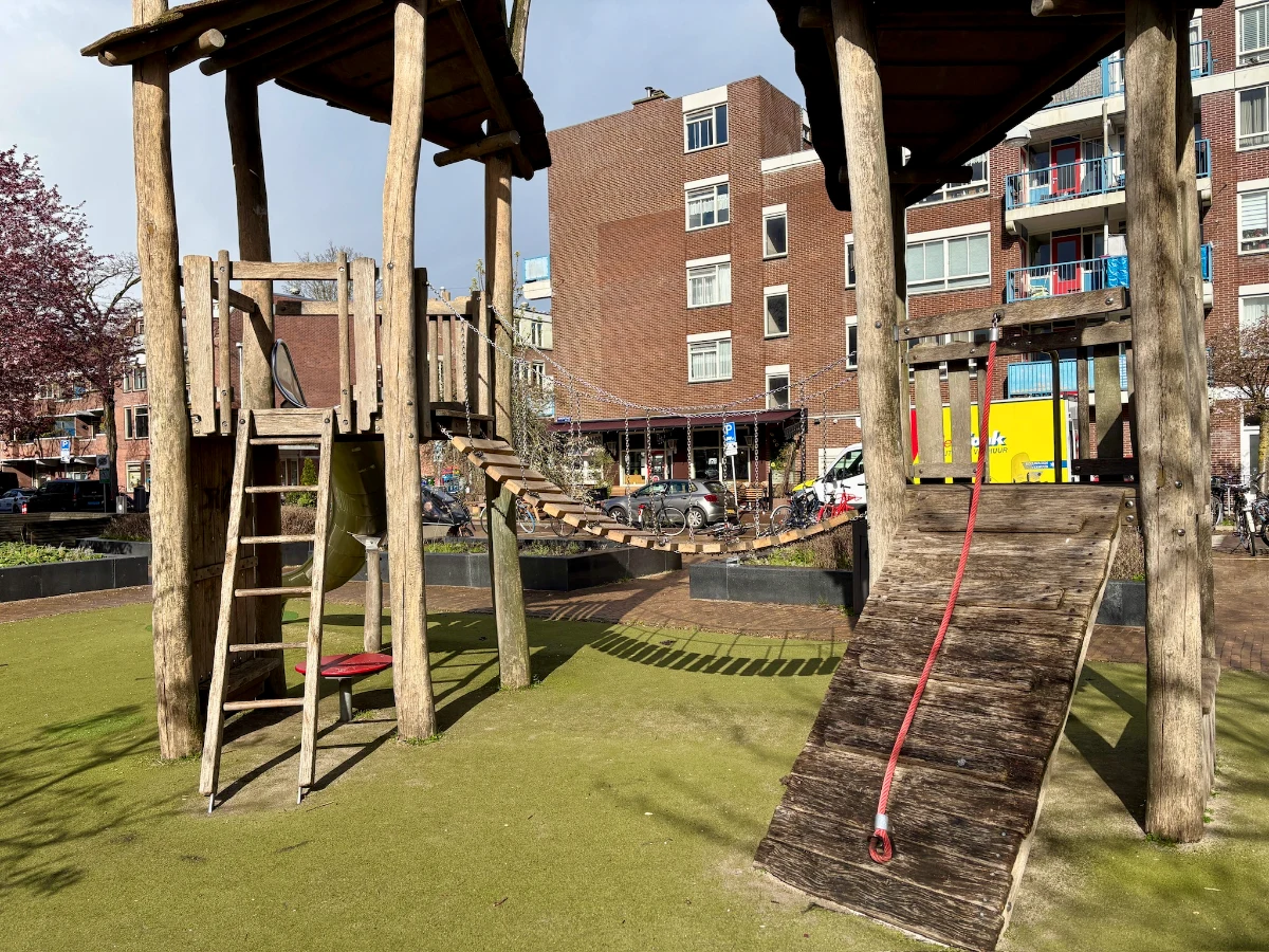 Wooden playground structure with two towers connected by a bridge and ladders and rope pull