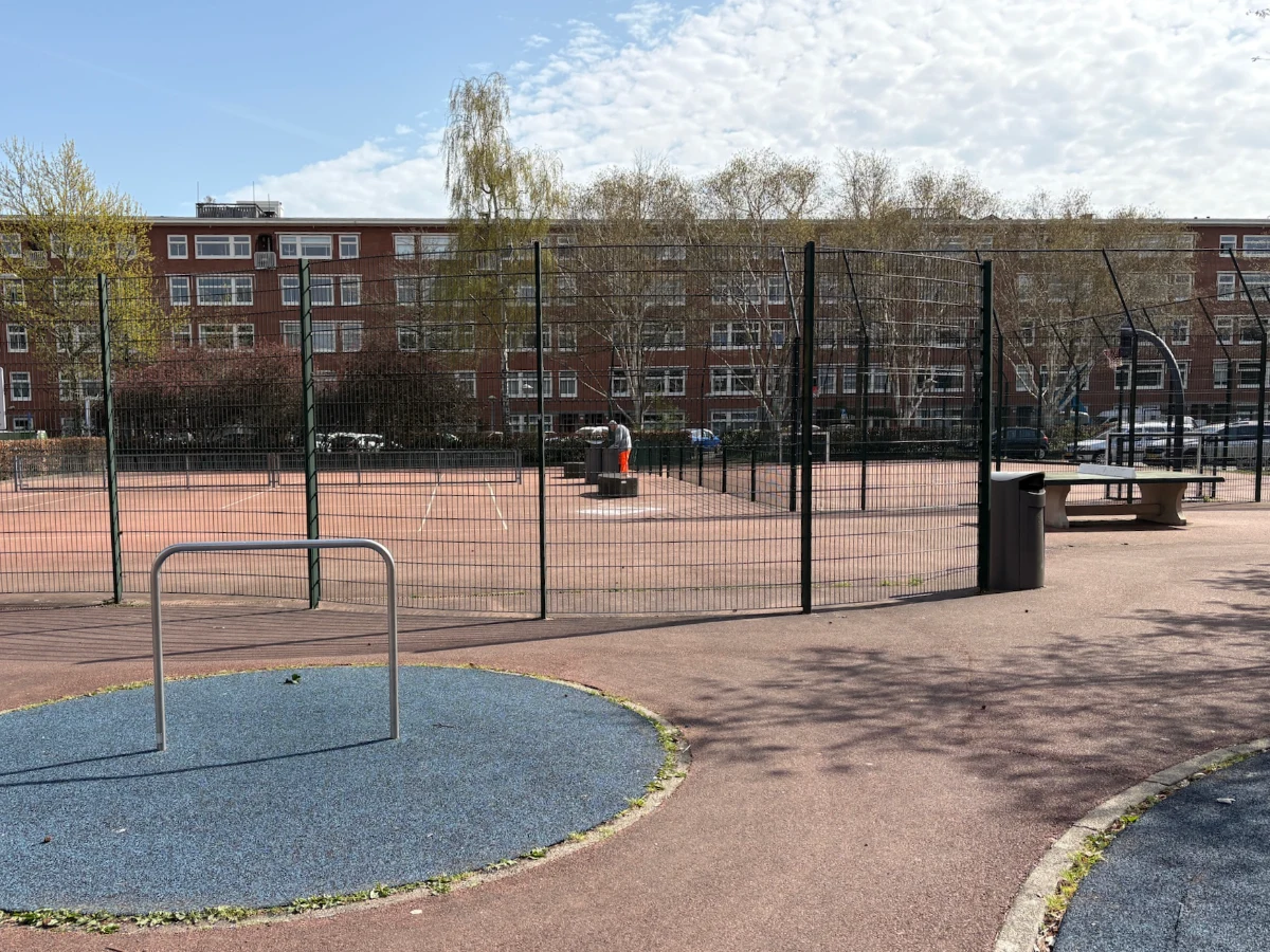 Tennis court and football pitch behind metal enclosure in urban setting