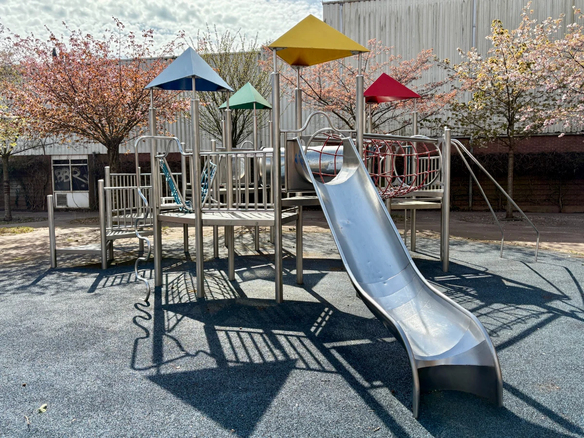 Metal climbing structure with slide and bright blue, yellow, red, and green pyramids on top