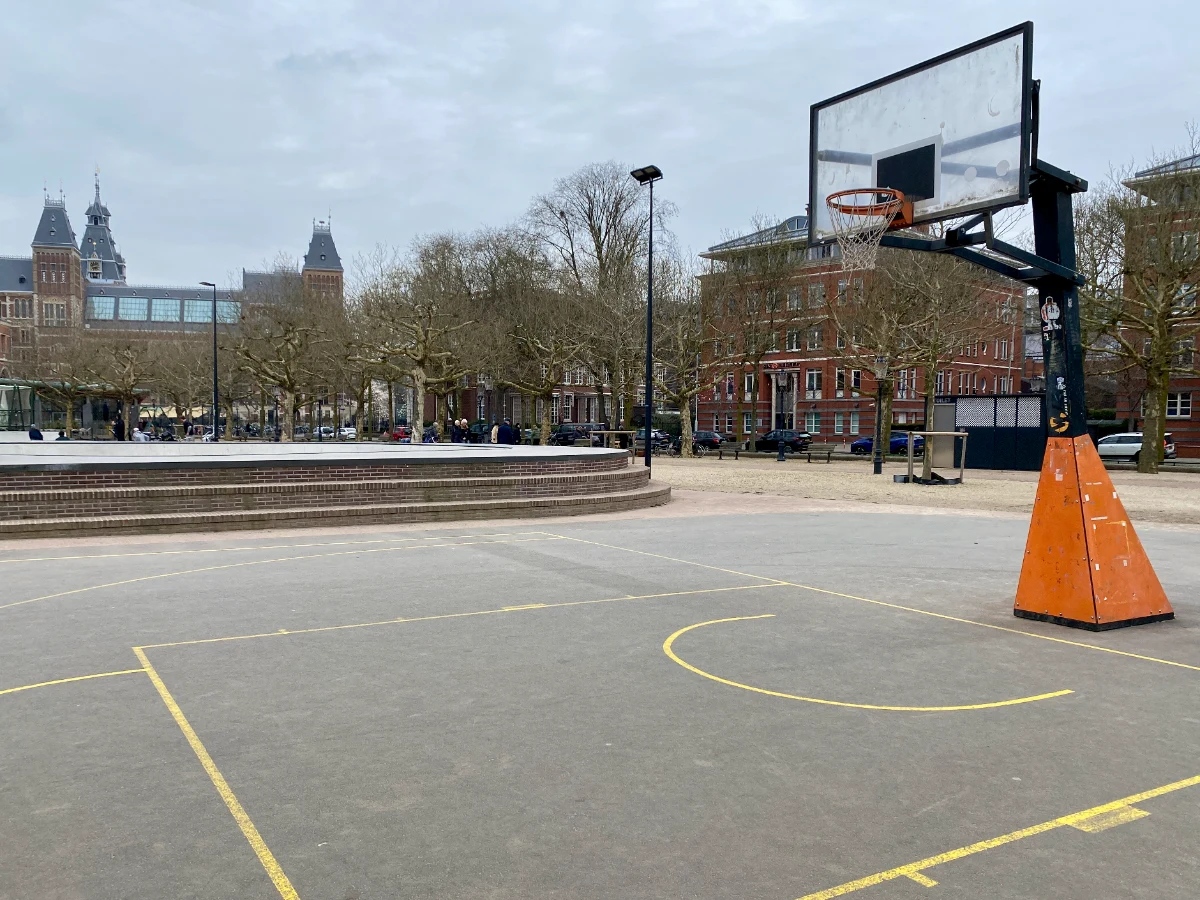 Basketball court with concrete and yellow lines and basketball hoop with museum in ditance