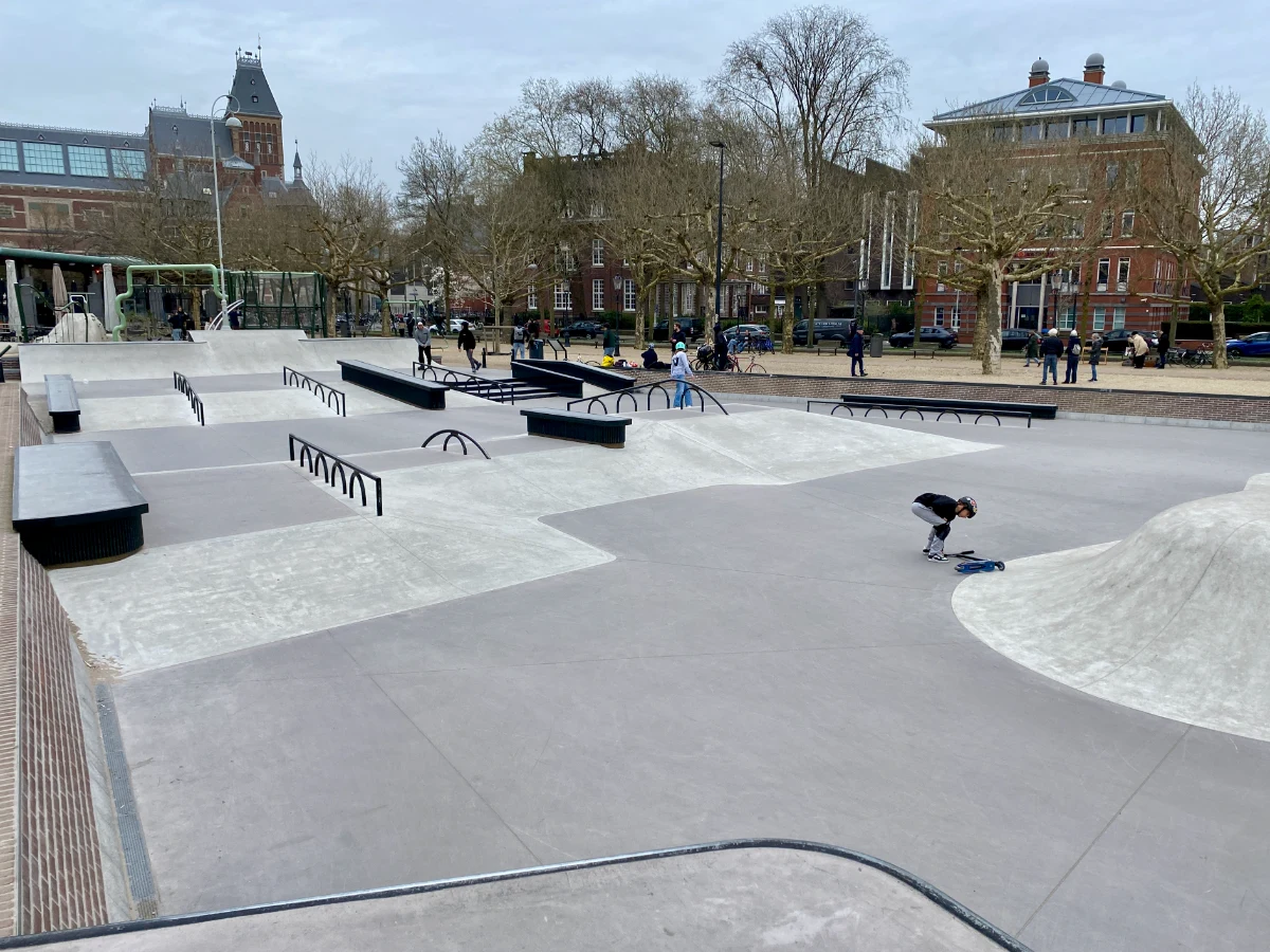 Kids at skatepark with ramps, rails, ledges and trees and buildings behind