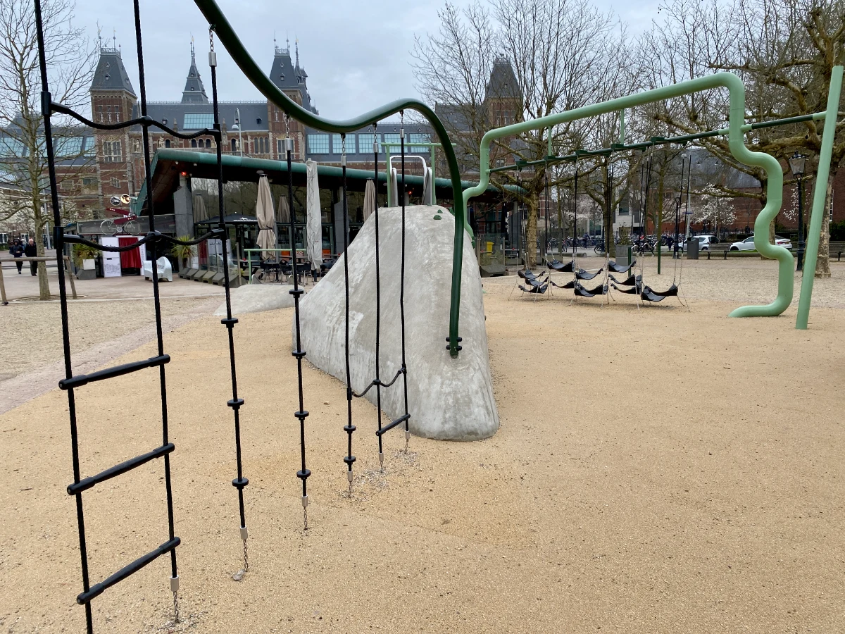 Modern playground in large city plaza with rope ladders and green frame with hammock obstacle course