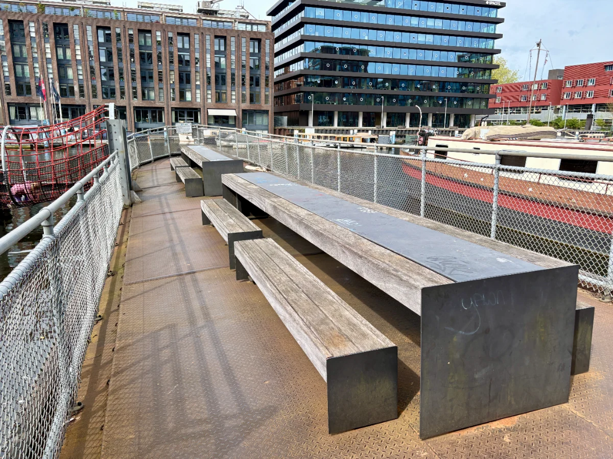 Barge with three long wooden picnic tabls and benches and other boats and buildings seen behind
