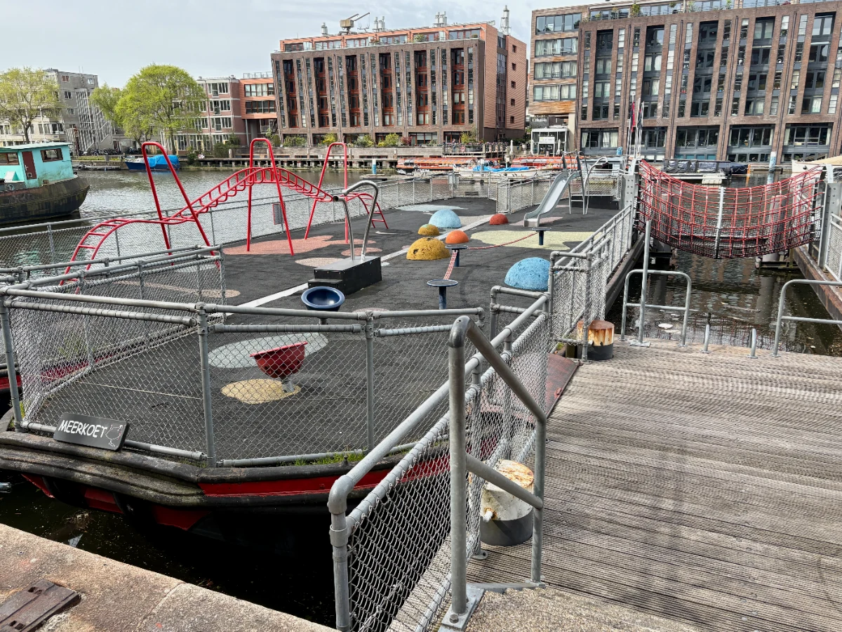 Stairs leading to barge playground with red, blue, yellow, and orange play equipment and red rope bridge