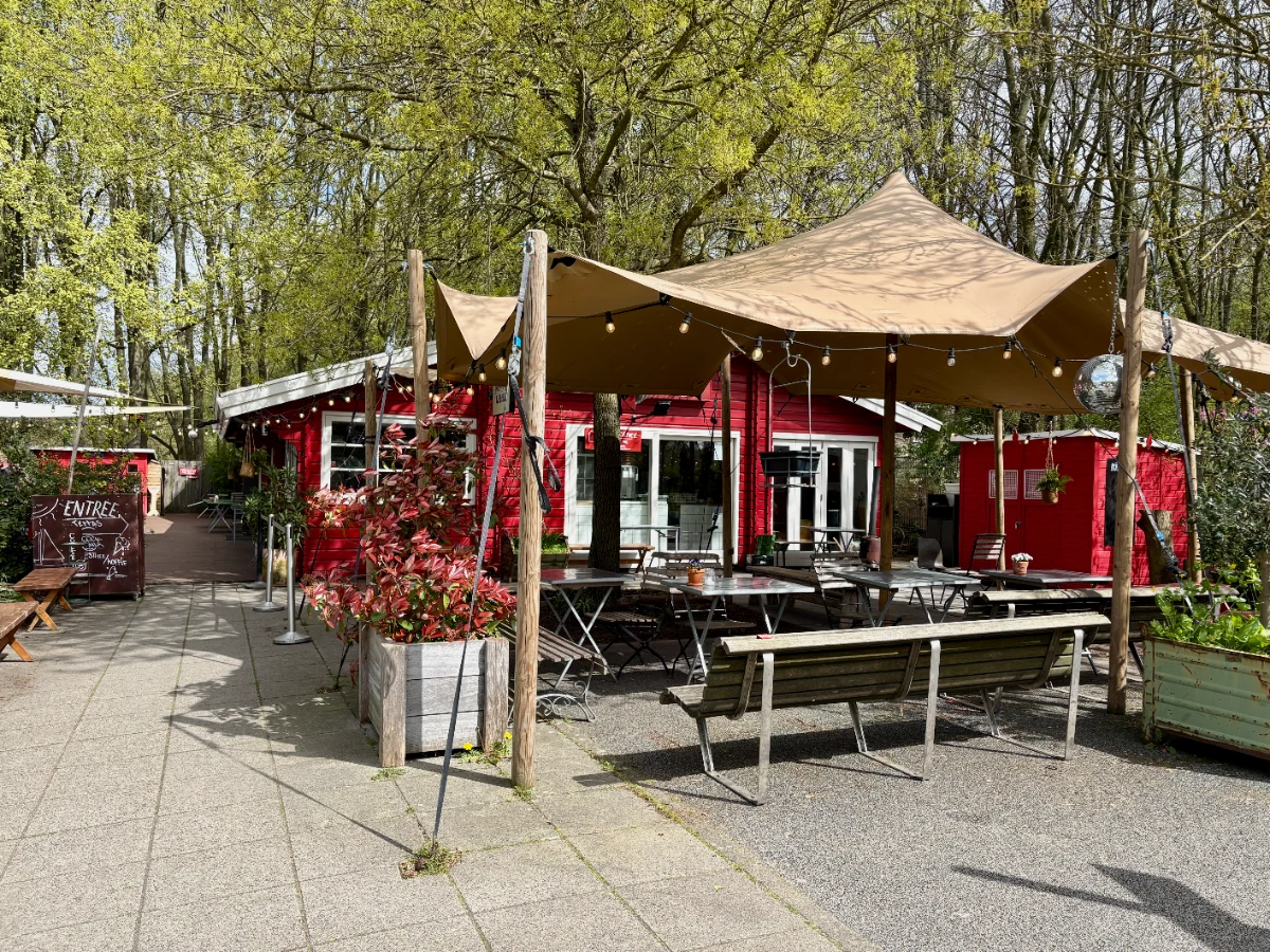 Red=painted restaurant with large canopy covering terrace with outdoor seating and trees