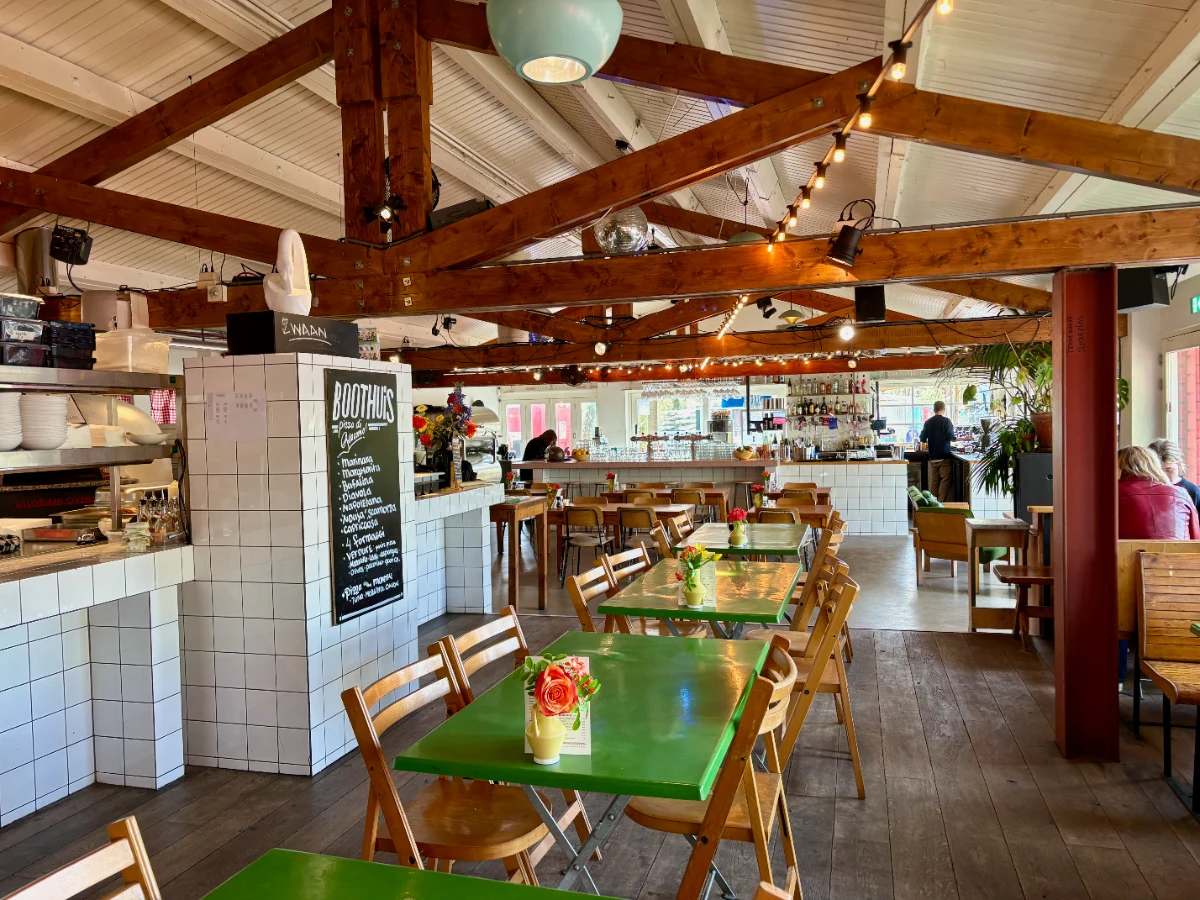 Restaurant interior with white-tiled counter, green tables, and vaulted ceilings with wooden beams