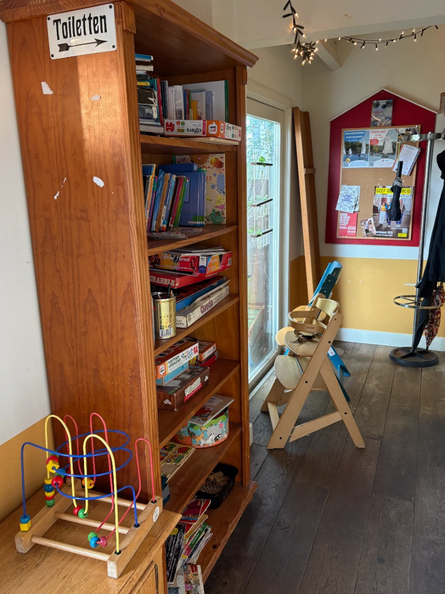 Wooden bookcase with toys, books, and games next to a high chair