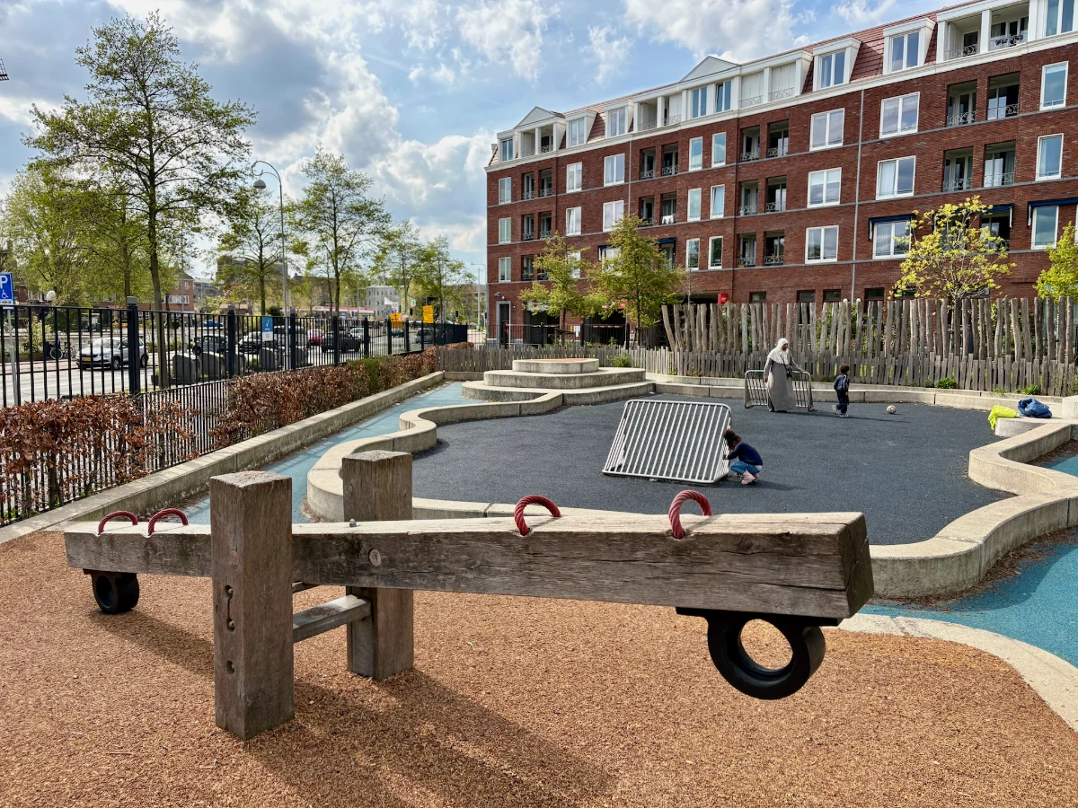 Mom and kids play on small football pitch with curvy concrete edges with wooden seesaw in front