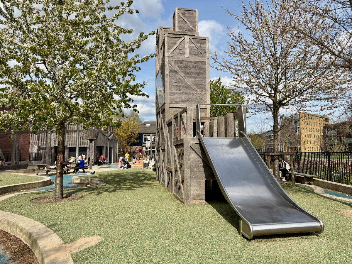 Wooden crate play tower with wide slide and community building behind