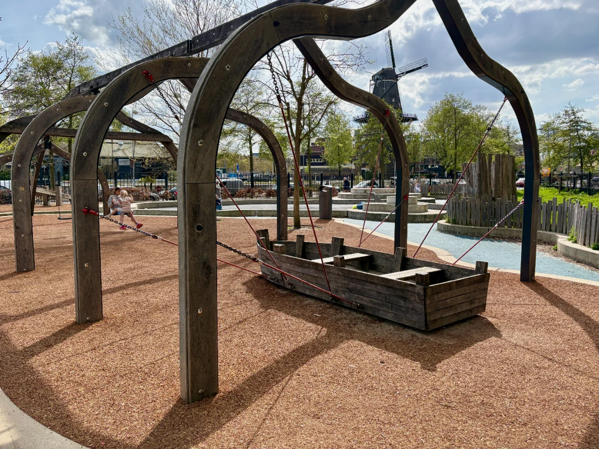 Curved wooden frame supporting rocking boat with windmill in the distance