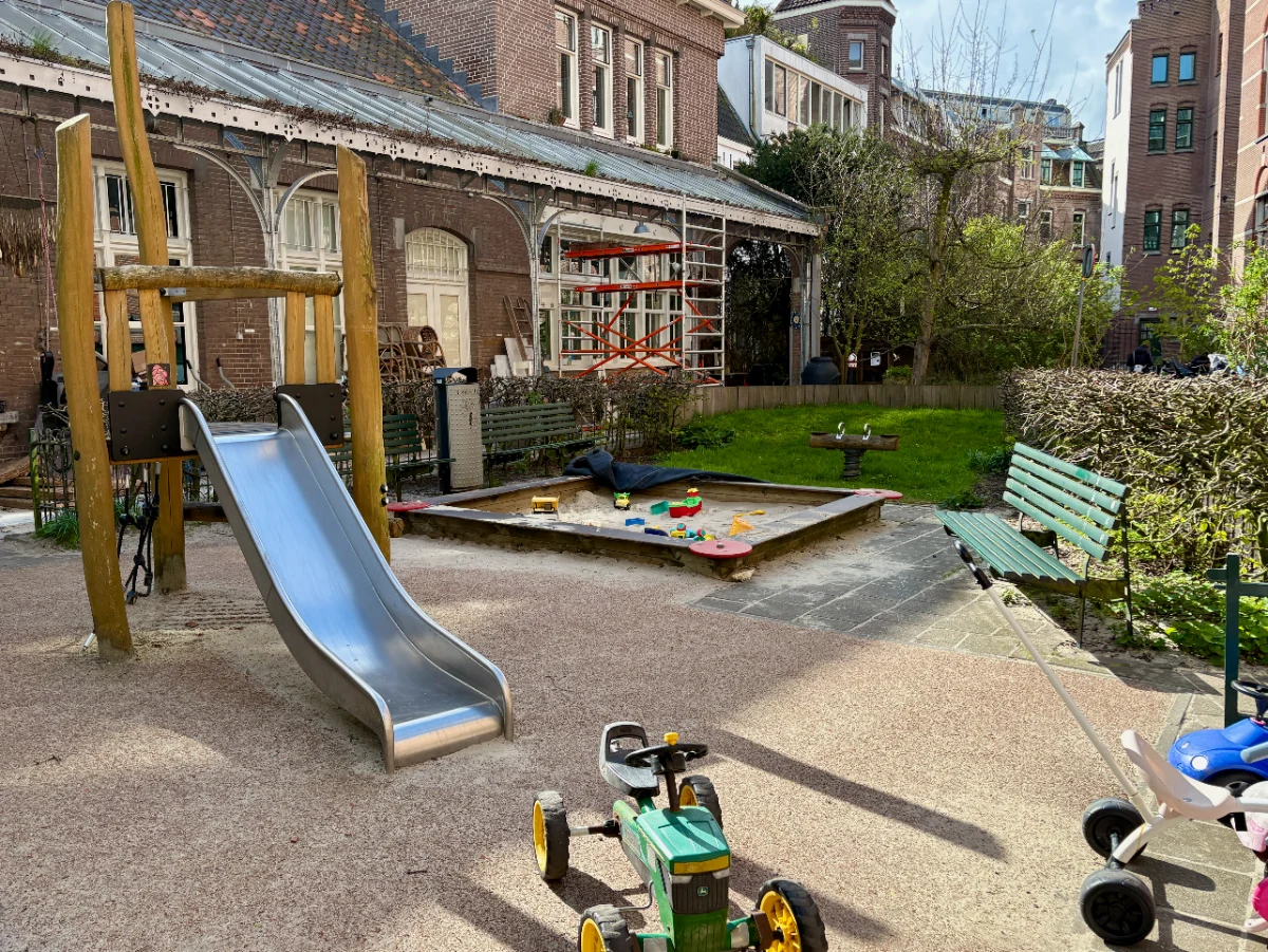 Small wooden climbing structure with slide alongside a sandbox with toys, green bench, and green lawn