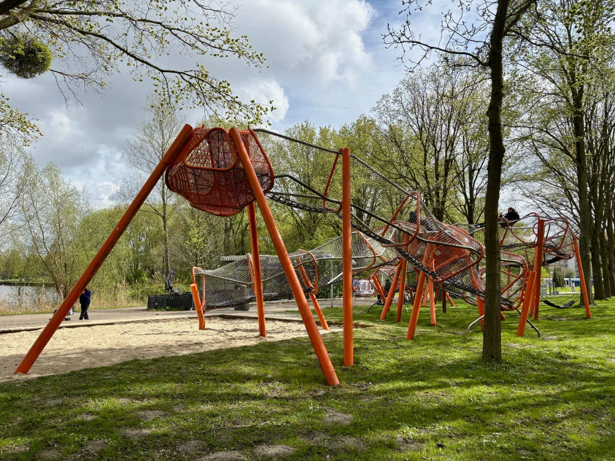 Modern orange play structure with undulating rope course enclosed with metal mesh
