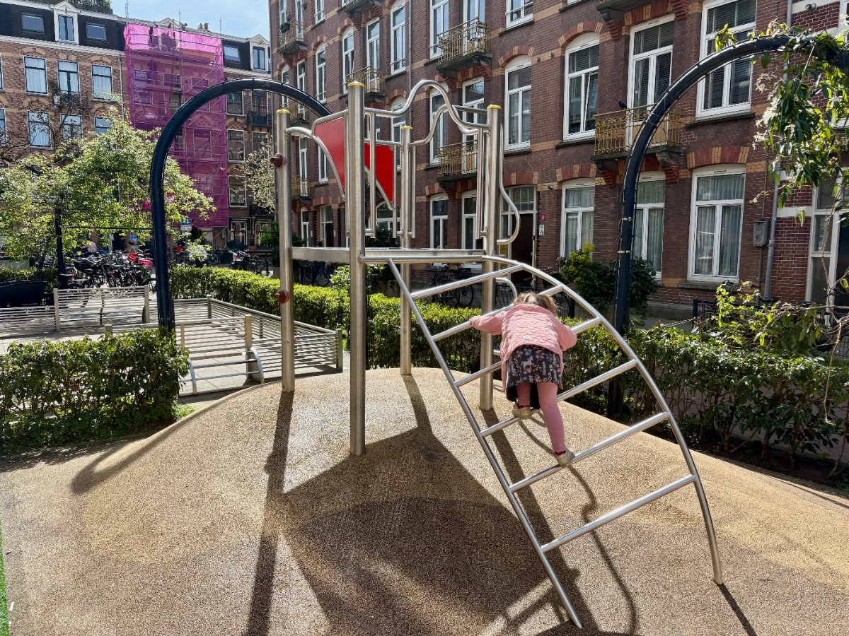 Girl climbing ladder of modern metal climbing structure with mini football pitch behind