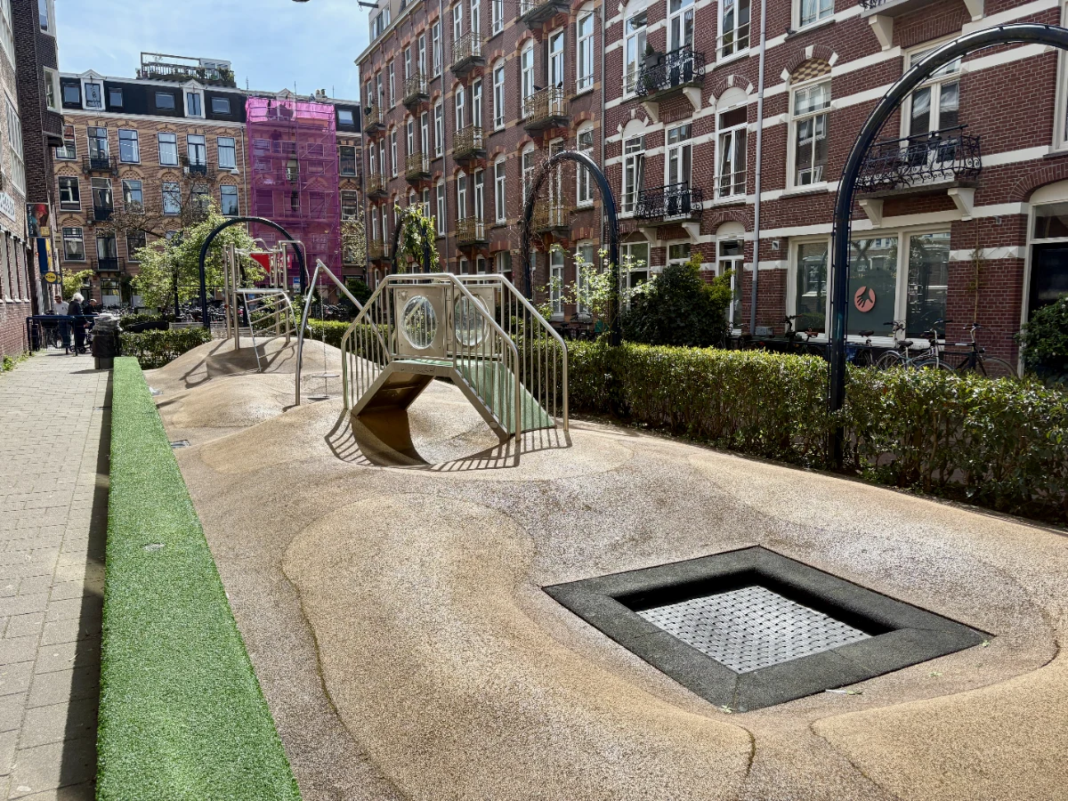 Undulating playground with trampoline and climbing structures and residential buildings behind