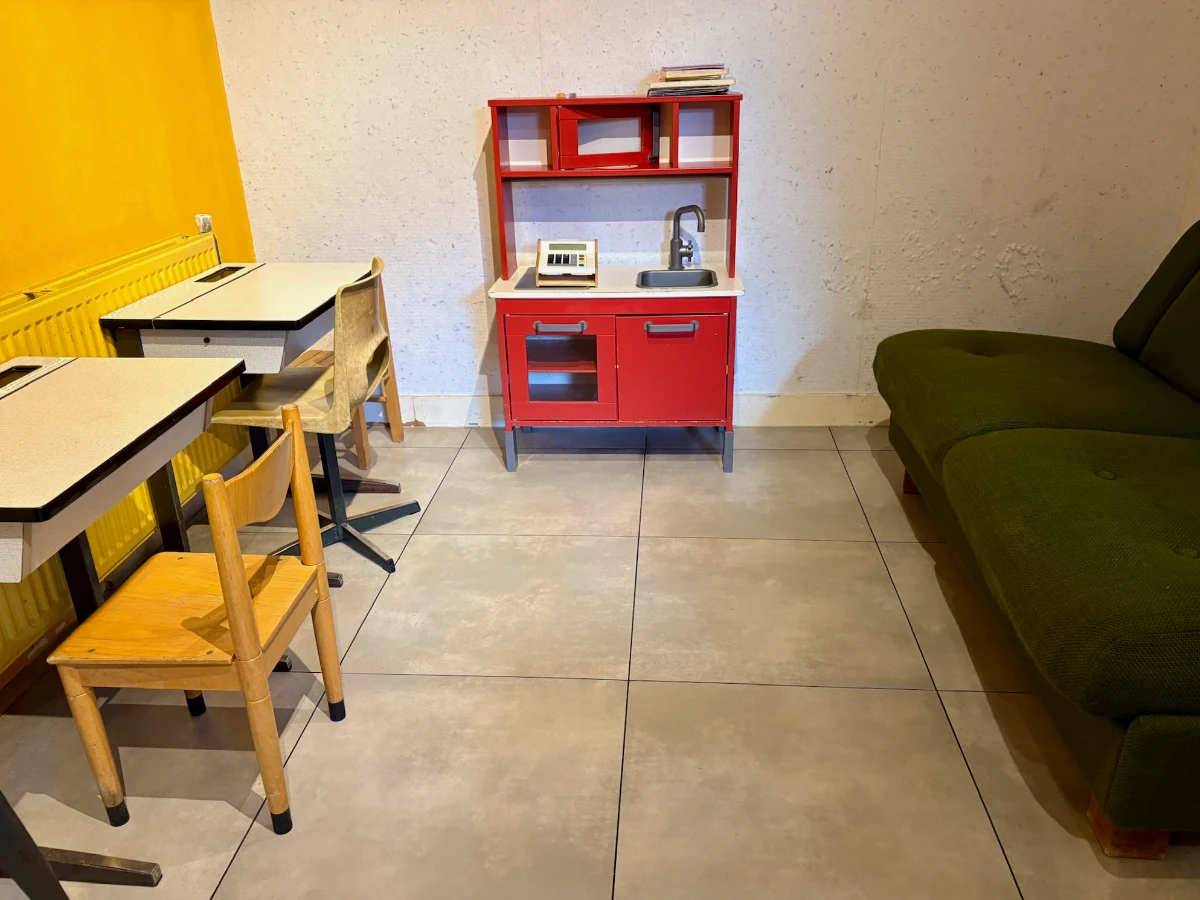 Small basement play area with children's desks, chairs, red play kitchen, and a cough