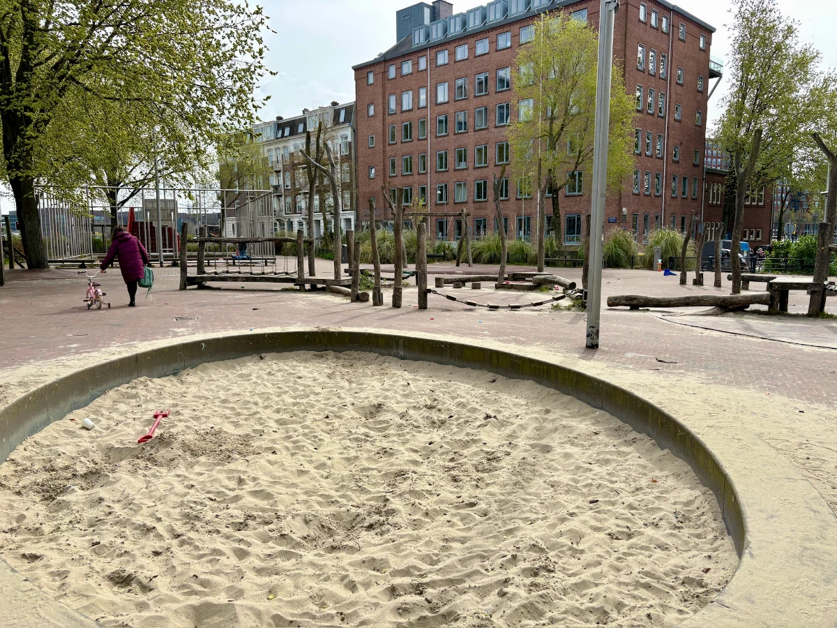 Round sand box with wooden play structures and tall residential buildings behind