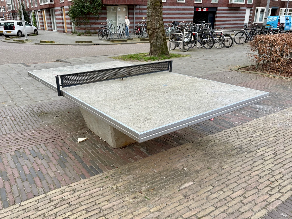 Concrete table tennis table with black net and bikes and buildings behind